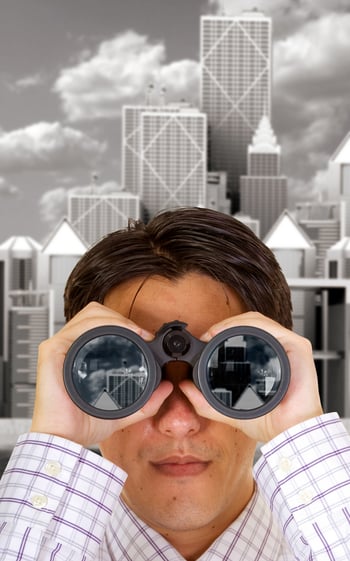 businessman with binoculars with a corporate district in the background - buildings reflections on lenses